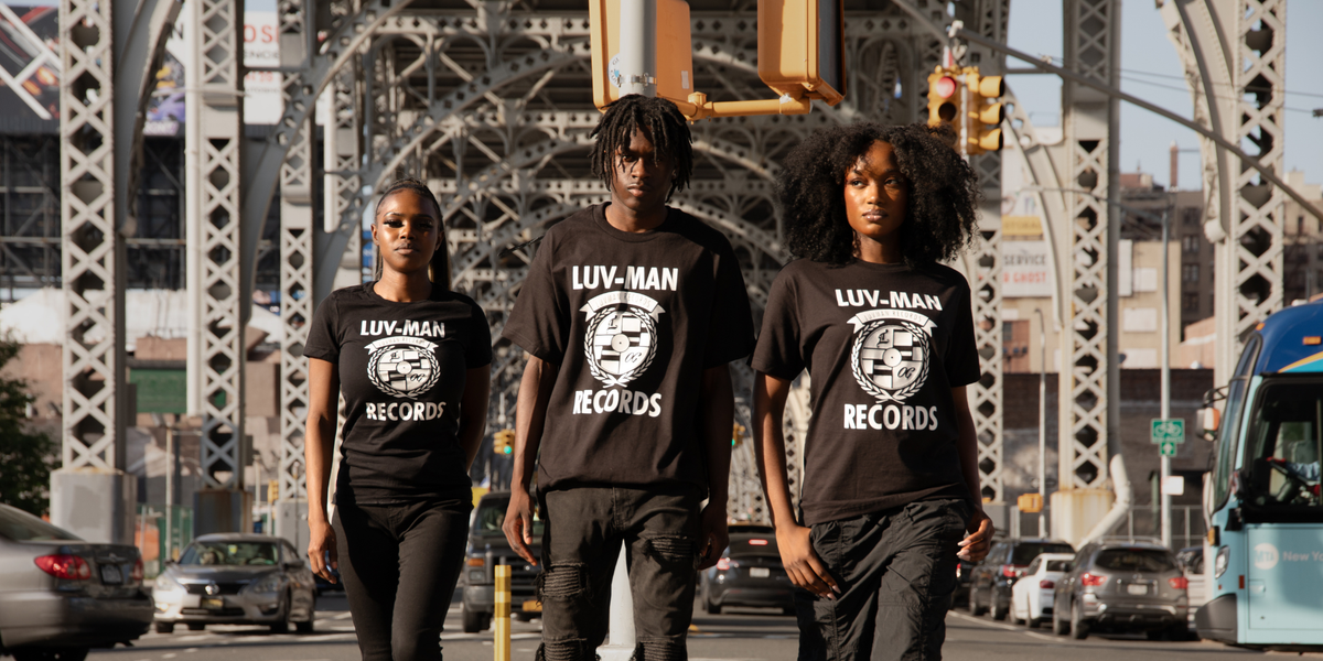 Three people wearing black t-shirts with 'Luv-Man Records' printed on them, standing on a city street.